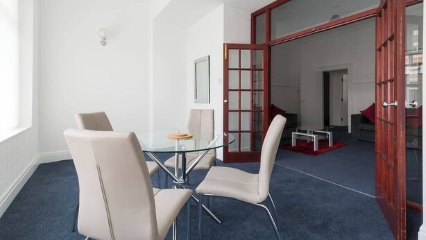 A modern conference room with a glass table, white chairs, and a red door leading to another room. - Two-Bedroom Apartment Ground Floor (Blackpool)