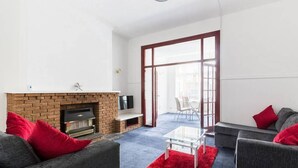 A modern living room with a brick fireplace, grey sofas with red cushions, a glass coffee table, and a red rug. - Two-Bedroom Apartment Ground Floor (Blackpool)