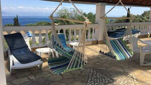 A covered outdoor seating area with two hanging hammocks and a white chair.