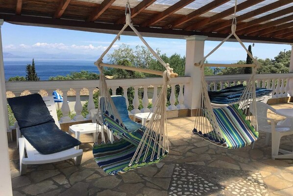 A covered outdoor seating area with two hanging hammocks and a white chair.