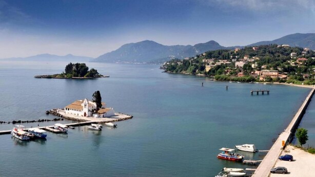 A coastal town with a marina, a small island with a white building, and mountains in the background.