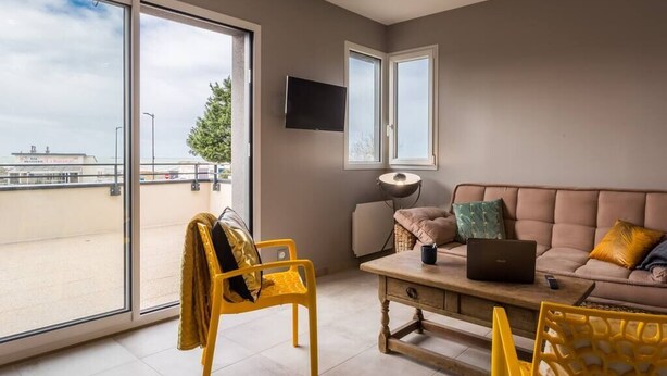 A room with a sofa, a yellow chair, a table with a laptop, and a TV on the wall. - Tribord, apartment with terrace and sea view, parking (Saint-Côme-de-Fresné)