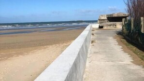 A concrete walkway beside a beach with a clear view of the ocean. - Tribord, apartment with terrace and sea view, parking (Saint-Côme-de-Fresné)