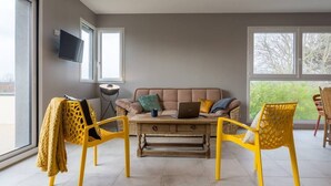A modern living room with a beige sofa, yellow chairs, a wooden coffee table, and a TV mounted on the wall. - Tribord, apartment with terrace and sea view, parking (Saint-Côme-de-Fresné)