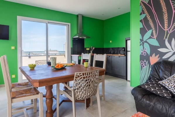 A dining area with a wooden table and chairs, a kitchen with a black countertop, and a green wall.