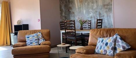 A living room with two brown leather sofas, a dining table with chairs, and a decorative wall.