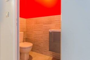 A bathroom with a white toilet, a sink, and a tiled wall. - La Proue, Appt Avec Terrasse à 60m de la mer (Saint-Côme-de-Fresné)