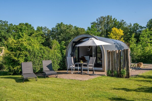 Eine moderne Außenarchitektur mit gewölbtem Dach, einem Tisch mit Stühlen und einer Glastür zum Innenbereich.