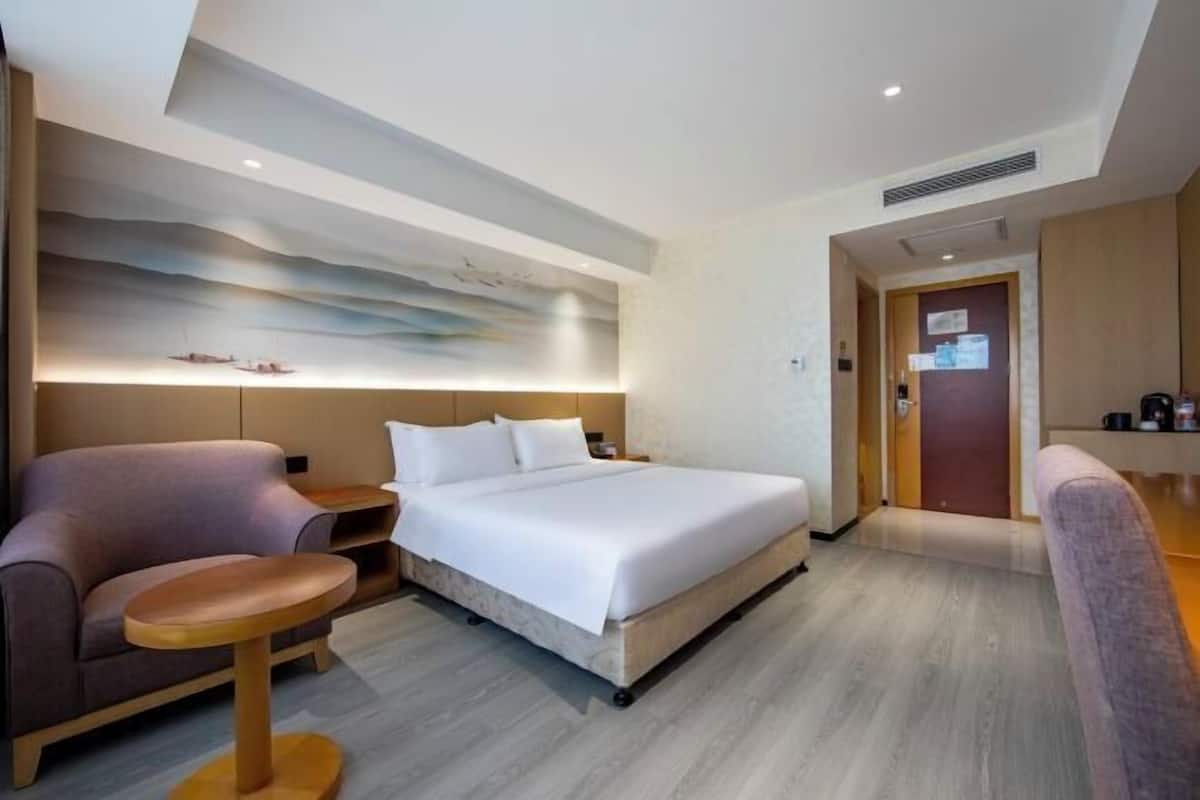 A modern hotel room with a bed, a sofa, a small table, and a wall-mounted artwork.