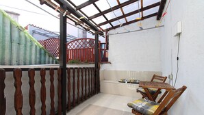 A covered patio area with a wooden bench and a table, a red gate, and a view of a building with a red fence. - Apartment 2178/55780 (Istria - Pula), 3000m from the beach (Pula)