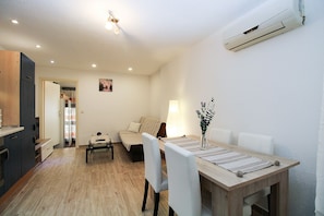 A compact living space with a dining area, a sofa, a lamp, and a wall-mounted air conditioner.