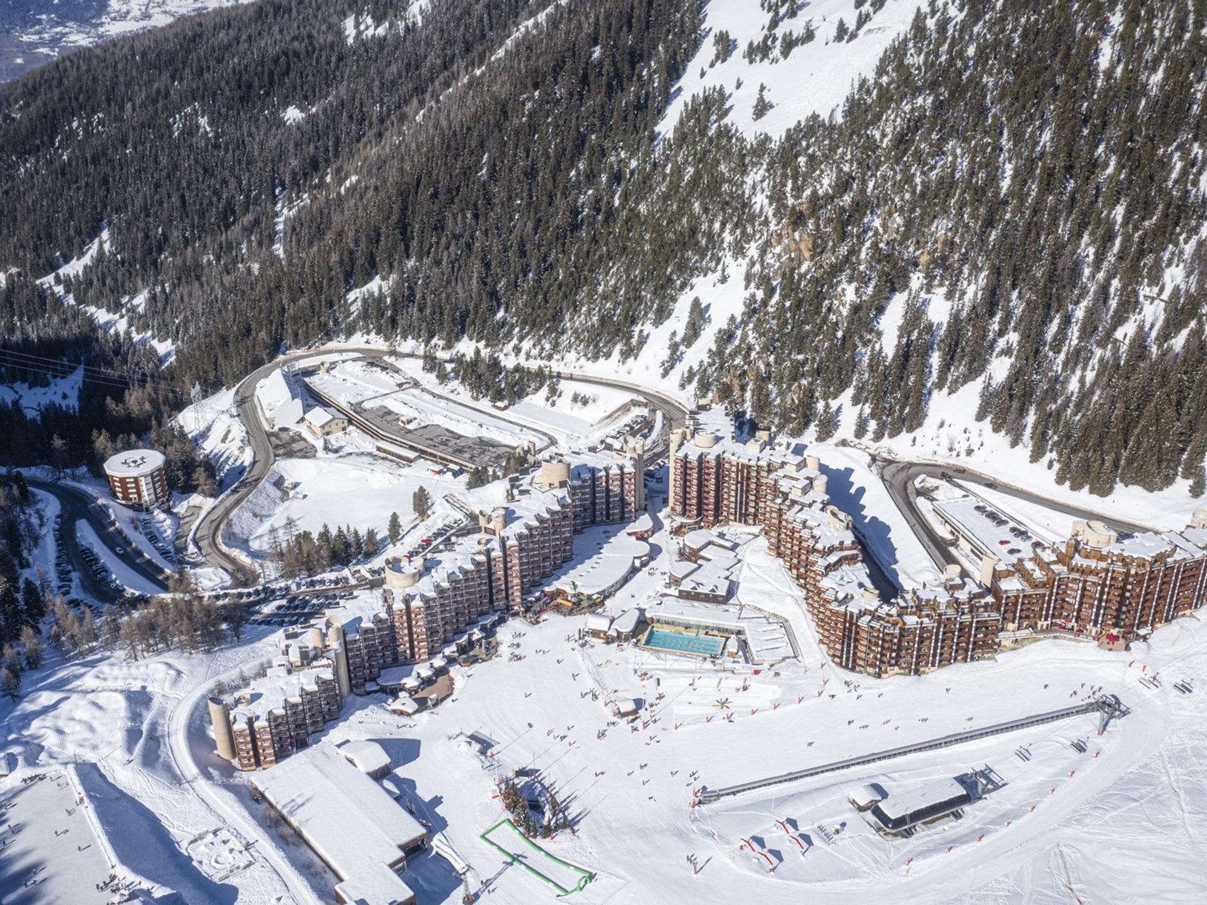 A snow-covered ski resort with multiple buildings, a swimming pool, and ski slopes.