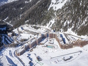 A snow-covered ski resort with multiple buildings, a swimming pool, and ski slopes.