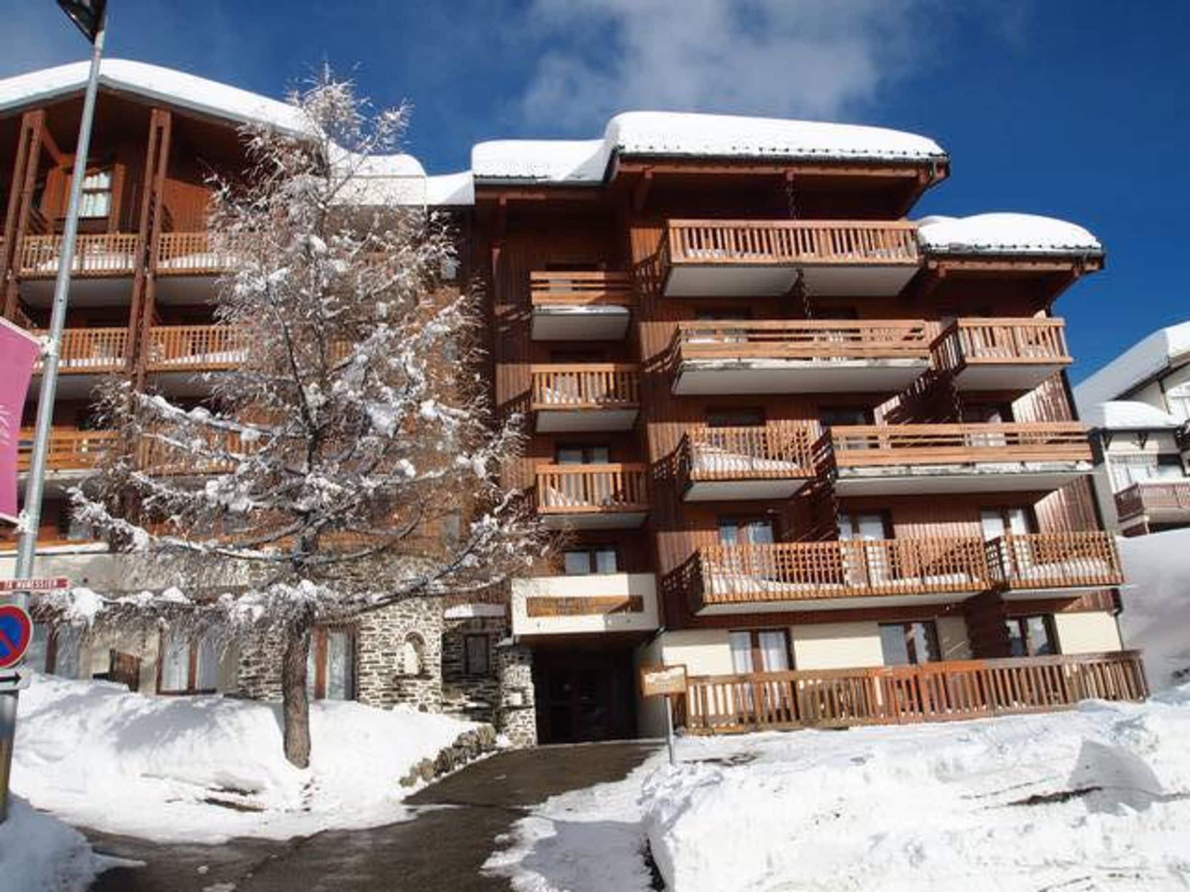Un immeuble à plusieurs étages doté de balcons, un arbre recouvert de neige et un ciel dégagé.