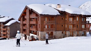 Un edificio de madera de varios pisos con balcones, pistas de esquí al frente y montañas nevadas al fondo.