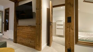 Un interior moderno con paneles de madera, un televisor montado, un radiador blanco y una cama con cabecera de vidrio.
