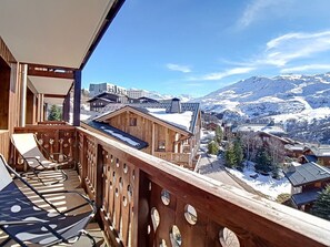 Un balcón de madera con vistas a montañas nevadas y un pueblo en la falda.