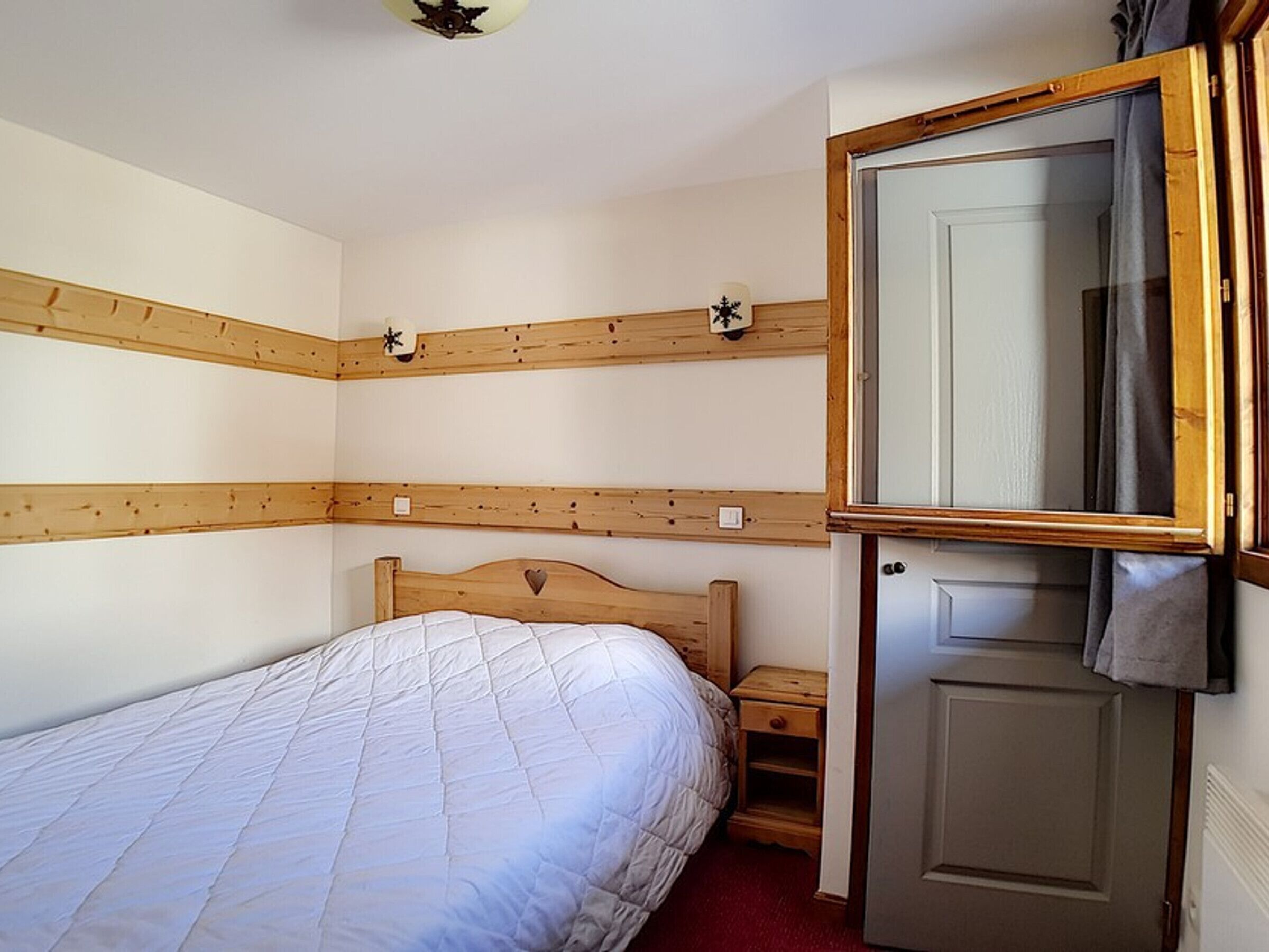 A bedroom with a wooden headboard, a bed with a quilt, a nightstand, a mirror, and a door.