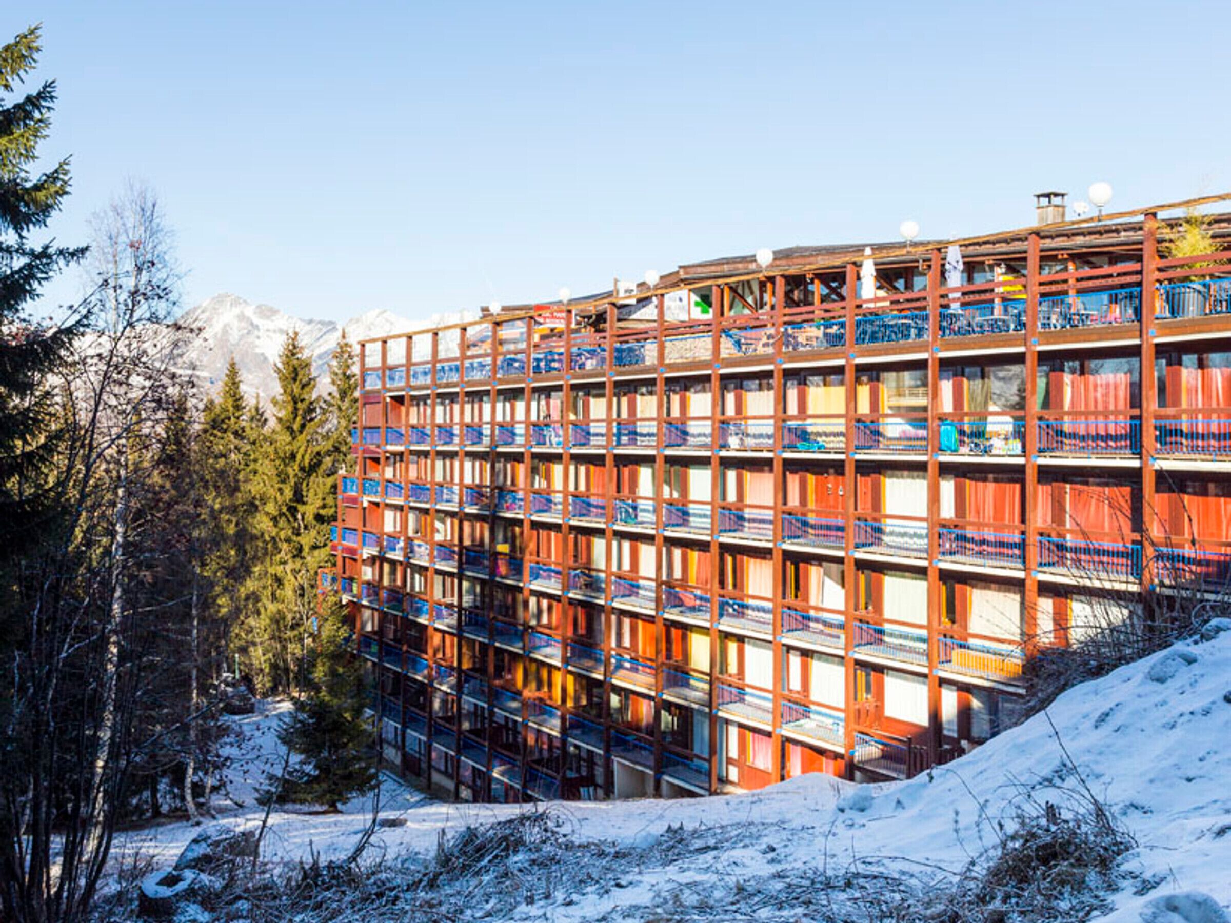A multi-story building with a metal framework and colorful panels, surrounded by snow and trees.