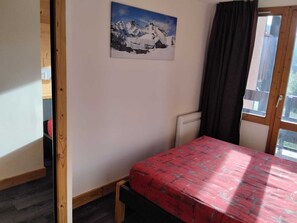 Een kamer met een bed, een raam, een berglandschap op een schilderij en een deur.