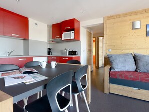 Een moderne keuken met rode kastjes, een eethoek met tafel en stoelen, en een houten wand met een bank.