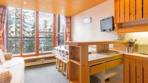 A cozy cabin interior with wooden walls, a dining area, and a large window offering a view of trees. - Renovated duplex in quiet area with balcony - 6/7 pers. (Les Arcs 1800)