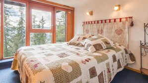 A bedroom with a large window, a bed with a quilt, and a wall-mounted light fixture. - Renovated duplex in quiet area with balcony - 6/7 pers. (Les Arcs 1800)