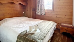 Ein Schlafzimmer einer Holzhütte mit einem Bett, einem Fenster mit Vorhängen und einem kleinen Tisch mit zwei Tassen.