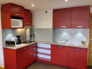 A compact kitchen with red cabinets, a microwave, a coffee maker, and a sink. - Spacious renovated apartment with parking and pets allowed (La Plagne Montchavin Les Coches)