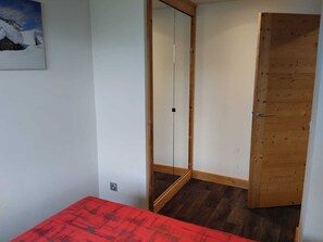 Una habitación con puerta de madera, un espejo y una colcha roja.