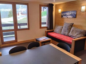 Una habitación con pared de madera, un sofá con cojines, una mesita y vistas a un paisaje montañoso a través de amplios ventanales.