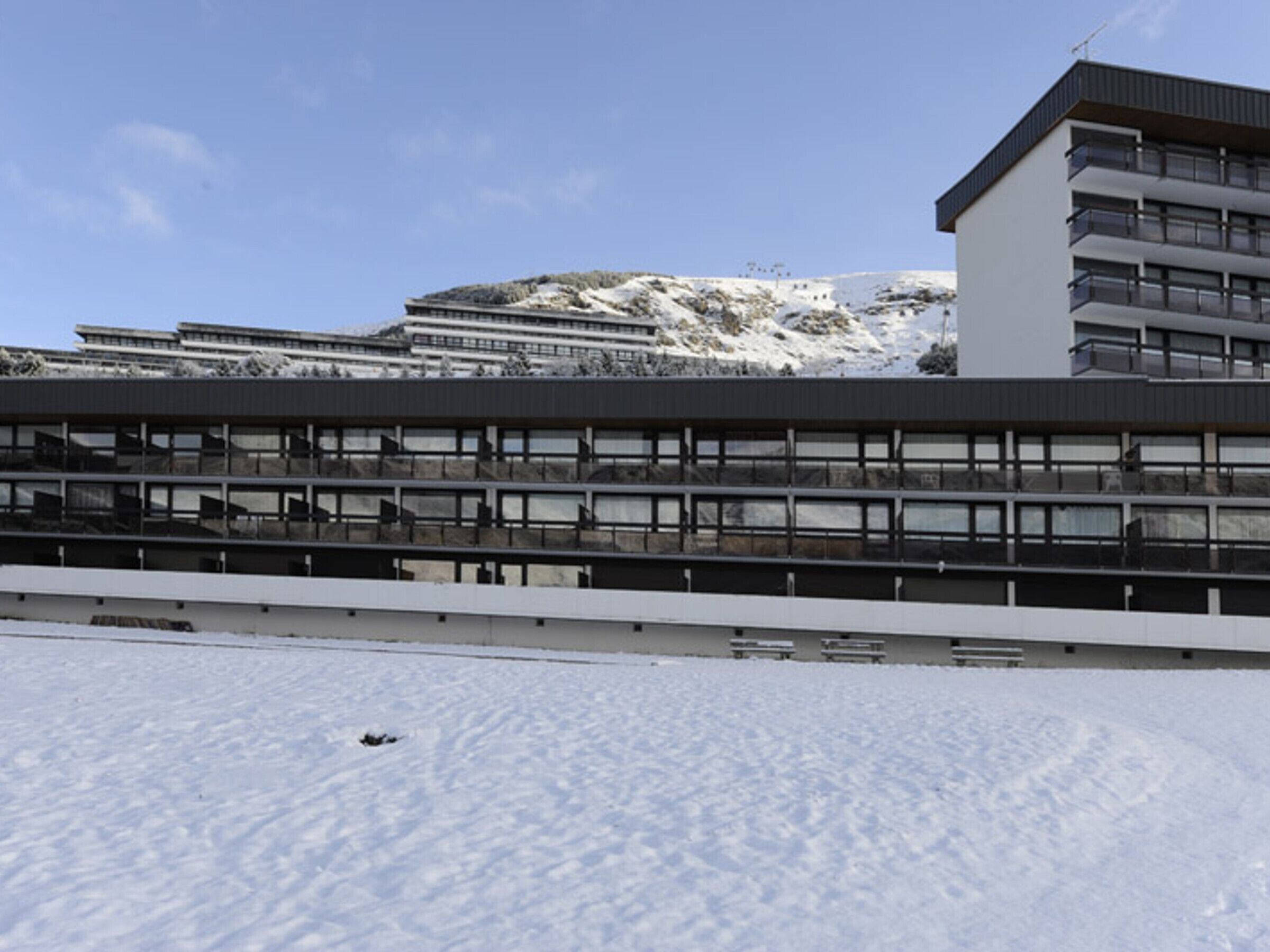Un bâtiment moderne à plusieurs étages, doté de grandes fenêtres, qui se détache sur un paysage enneigé avec une montagne en arrière-plan.