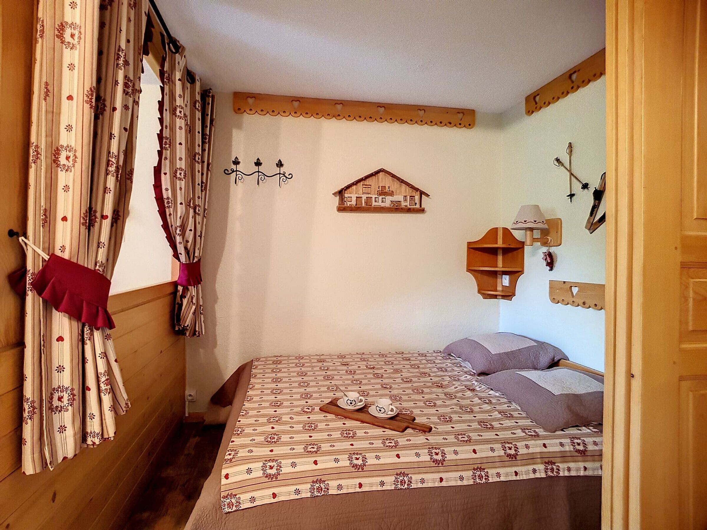 A cozy bedroom with a wooden headboard, a patterned bedspread, and a red curtain.
