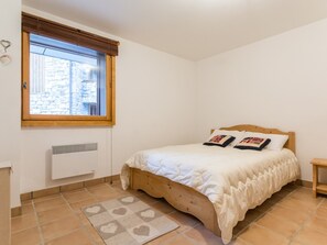 A bedroom with a wooden bed, a window with blinds, a radiator, and a patterned rug. - Spacious ski-in apartment with balcony and covered parking (La Rosière)