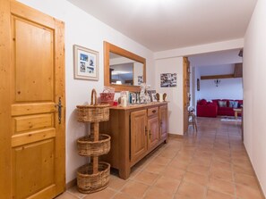 A hallway with a wooden door, a wicker basket, a mirror, and a red sofa in the background. - Spacious ski-in apartment with balcony and covered parking (La Rosière)