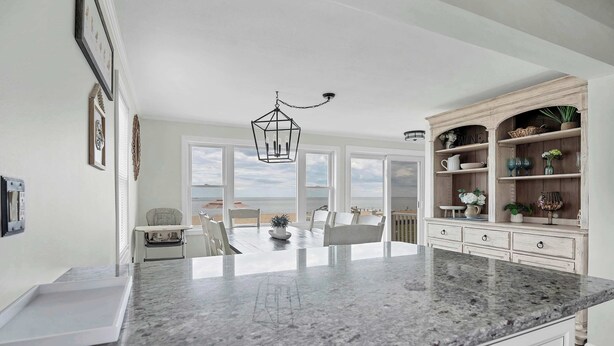 A kitchen with a marble countertop, white cabinetry, and a view of the beach. - Duckling Crossing | Beach House on the Sand (Westbrook)