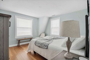 Un dormitorio con cama, mesita de noche, lámpara y ventana con persianas.
