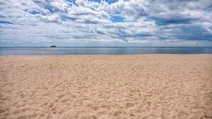 A beach with a sandy shore and a body of water in the background. - Duckling Crossing | Beach House on the Sand (Westbrook)