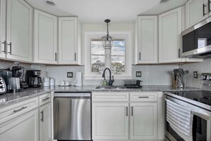 A modern kitchen with white cabinets, stainless steel appliances, a dishwasher, and a microwave. - Duckling Crossing | Beach House on the Sand (Westbrook)