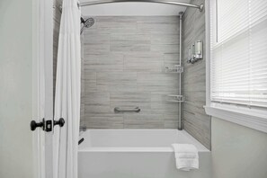 A modern bathroom with a shower, a bathtub, and a window with blinds. - Duckling Crossing | Beach House on the Sand (Westbrook)