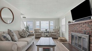 A living room with a sofa, chairs, a coffee table, a fireplace, and a TV. - Duckling Crossing | Beach House on the Sand (Westbrook)