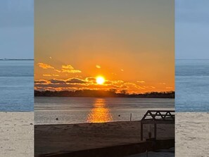 Un coucher de soleil sur une étendue d’eau, avec une jetée en bois et une rambarde.