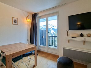 A room with a wooden table, a chair, a television, and a view of mountains through a sliding door.