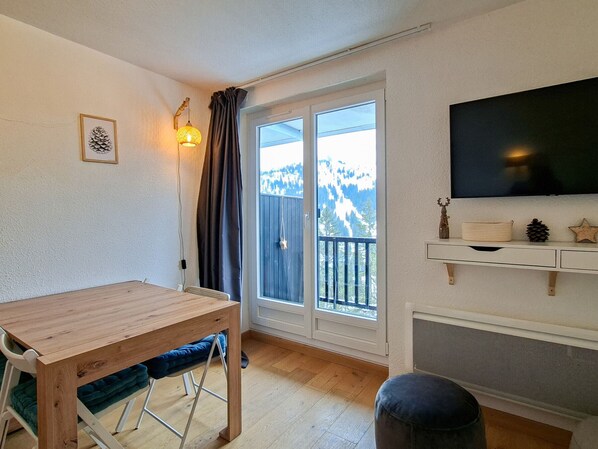 A room with a wooden table, a chair, a television, and a view of mountains through a sliding door.
