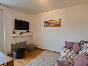 A living room with a flat-screen TV mounted on the wall, a fireplace below, a sofa with patterned cushions, and a rug on the floor.