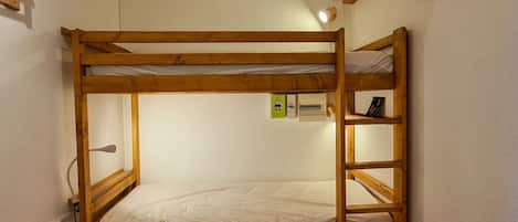 Un lit superposé avec une échelle, une prise de courant et une petite étagère sur laquelle se trouve un livre.