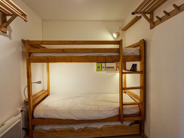 A bunk bed with a ladder, a power outlet, and a small shelf with a book.