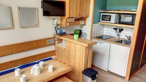 A compact kitchenette with a wooden table, a bench, a trash bin, a microwave, and a dishwasher.