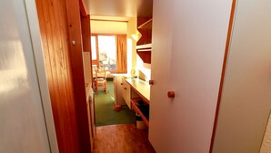 A narrow hallway with wooden walls and a green carpet leading to a kitchen area with wooden cabinets and a sink. - Ski-to-door studio with sunny balcony (Les Arcs 1800)
