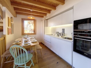 Uma cozinha moderna com armários brancos, um forno Siemens e uma área de refeições com mesa e cadeiras de madeira.